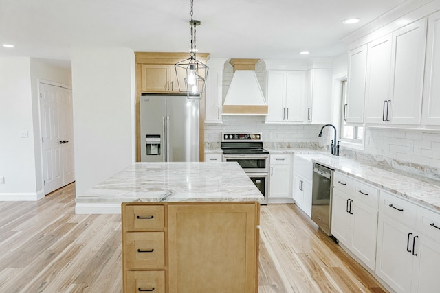 kitchen featuring stainless steel appliances, light wood-type flooring, custom range hood, and a sink