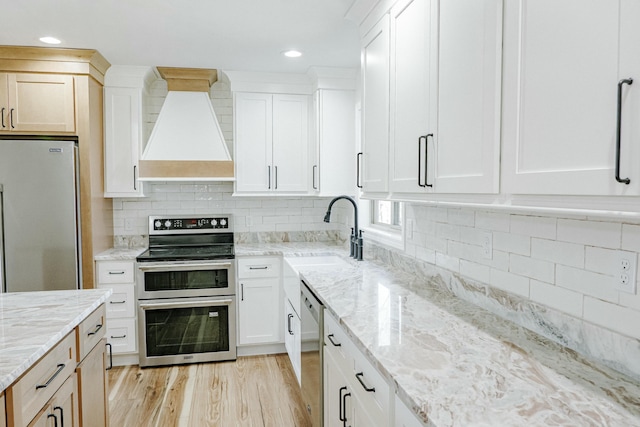 kitchen featuring light wood-style flooring, custom range hood, a sink, tasteful backsplash, and stainless steel appliances