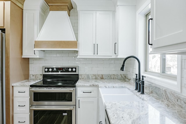 kitchen with premium range hood, white cabinets, and range with two ovens