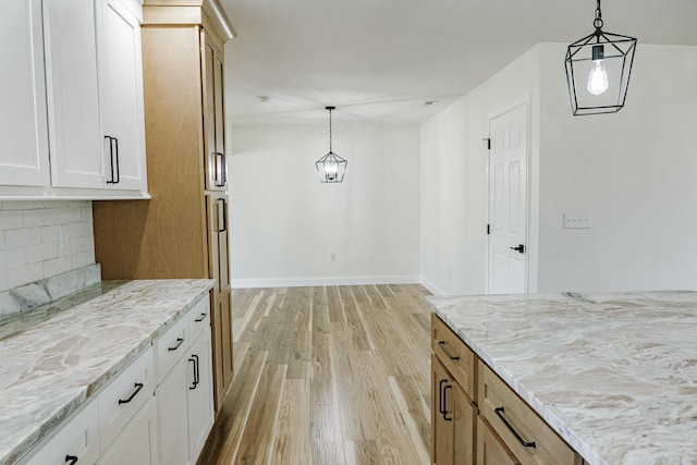 kitchen featuring light stone counters, decorative light fixtures, light wood finished floors, decorative backsplash, and baseboards