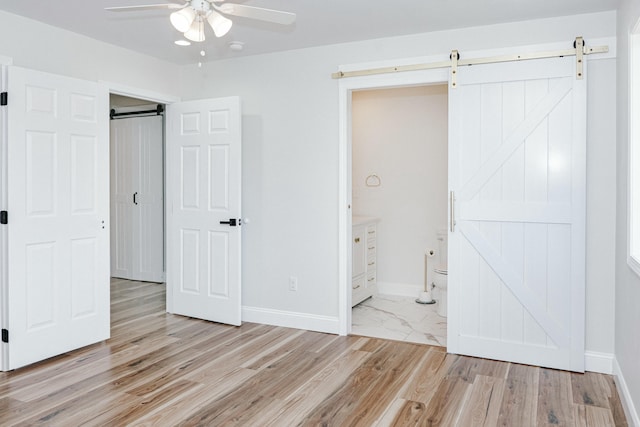 unfurnished bedroom with a barn door, light wood-style flooring, and baseboards