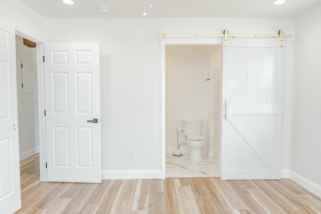 unfurnished bedroom with recessed lighting, a barn door, baseboards, and light wood-style flooring