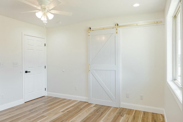 unfurnished bedroom with a barn door, baseboards, light wood-style floors, and a ceiling fan