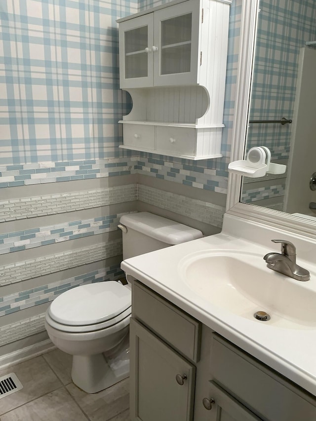 bathroom with toilet, wallpapered walls, visible vents, and vanity