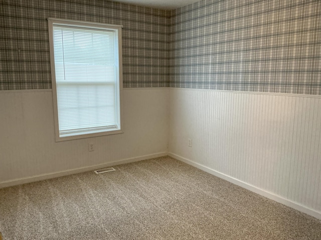 carpeted empty room featuring wallpapered walls and visible vents