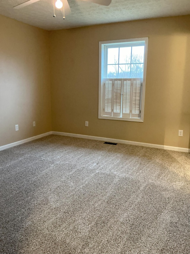 carpeted empty room featuring baseboards, a textured ceiling, visible vents, and a ceiling fan