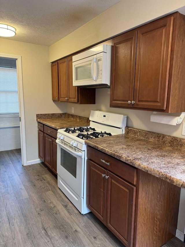 kitchen with a textured ceiling, white appliances, dark countertops, and dark wood finished floors