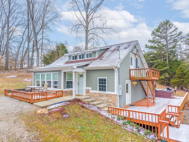 view of front of home with stone siding, roof with shingles, a hot tub, and a wooden deck