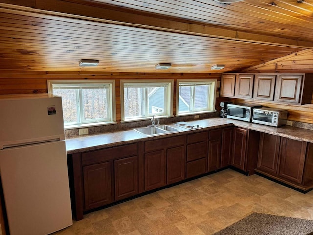 kitchen featuring freestanding refrigerator, stainless steel microwave, a sink, and dark countertops