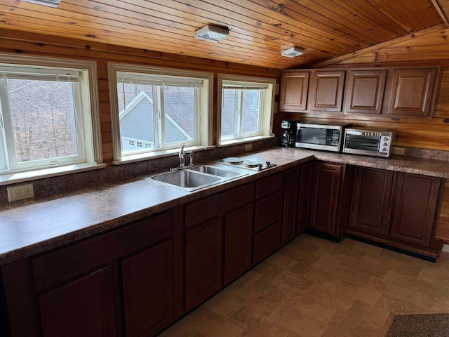 kitchen featuring lofted ceiling, a sink, wood ceiling, stainless steel microwave, and dark countertops