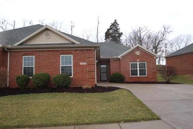 ranch-style house featuring a shingled roof, a front yard, and brick siding