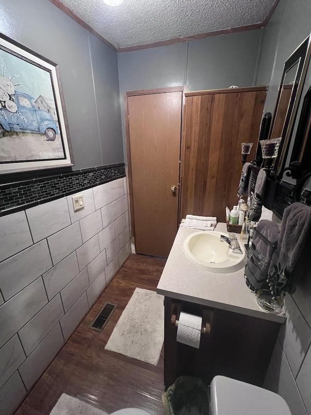 bathroom featuring a textured ceiling, wood finished floors, vanity, visible vents, and tile walls