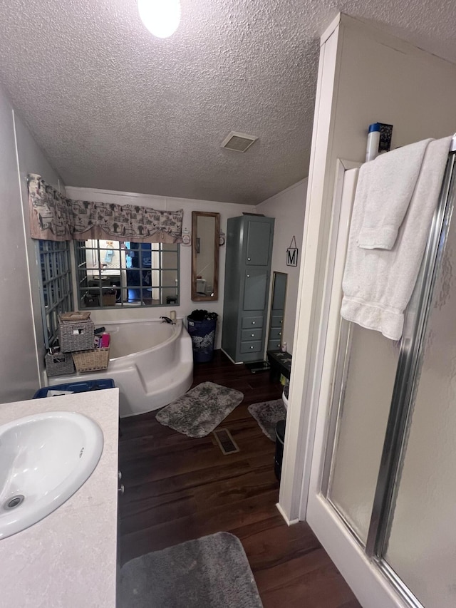 bathroom featuring a stall shower, vanity, a textured ceiling, wood finished floors, and a bath