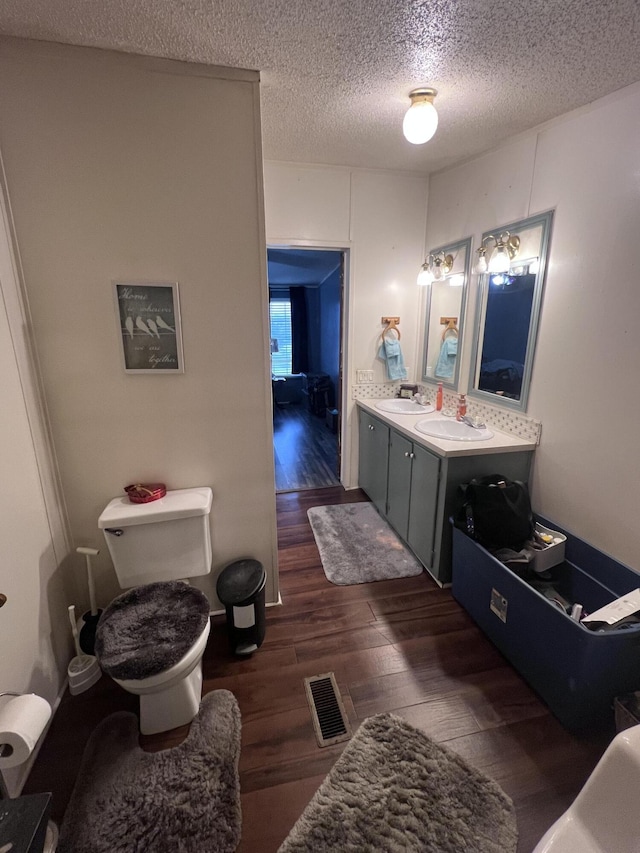 bathroom with visible vents, toilet, vanity, a textured ceiling, and wood finished floors