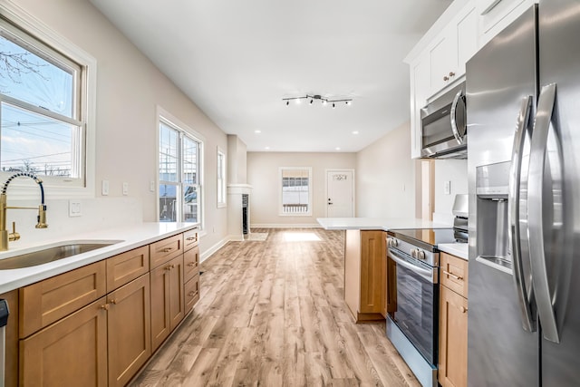 kitchen with stainless steel appliances, light wood finished floors, a sink, and light countertops