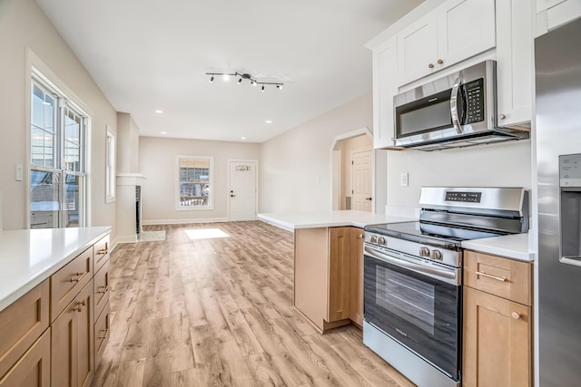 kitchen with arched walkways, light wood-style flooring, appliances with stainless steel finishes, open floor plan, and light countertops