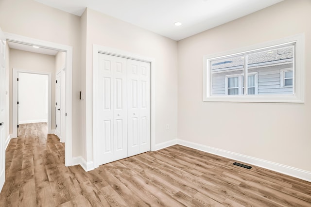 unfurnished bedroom with a closet, visible vents, baseboards, and wood finished floors