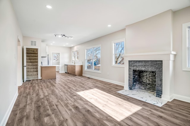 unfurnished living room with stairway, a fireplace with flush hearth, visible vents, and wood finished floors