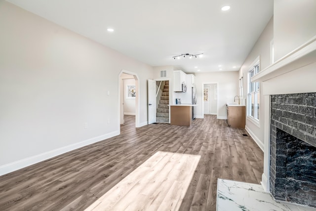 unfurnished living room featuring arched walkways, a fireplace, wood finished floors, baseboards, and stairs