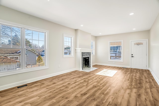 unfurnished living room featuring baseboards, a brick fireplace, visible vents, and light wood-style floors