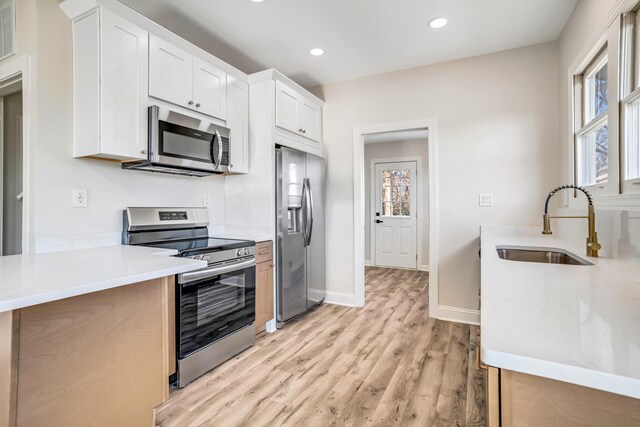 kitchen with recessed lighting, a sink, light countertops, appliances with stainless steel finishes, and light wood finished floors