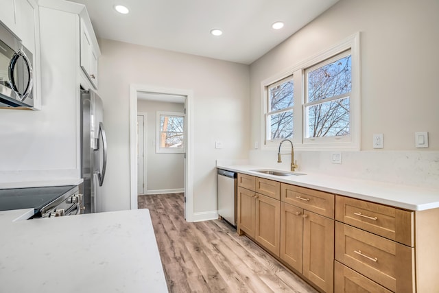 kitchen featuring stainless steel appliances, light countertops, light wood-type flooring, a sink, and recessed lighting