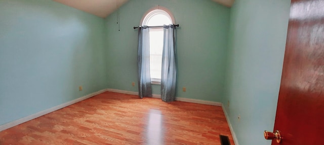 unfurnished room with vaulted ceiling, light wood finished floors, visible vents, and baseboards