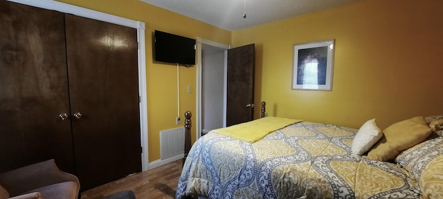 bedroom with a closet, wood finished floors, visible vents, and baseboards