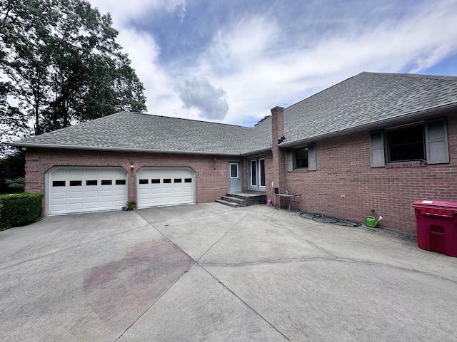 ranch-style home featuring a garage, driveway, brick siding, and roof with shingles