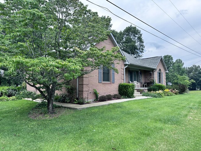 view of side of home with a yard, brick siding, and a shingled roof