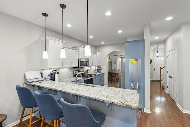 kitchen with arched walkways, appliances with stainless steel finishes, a kitchen bar, and light stone counters