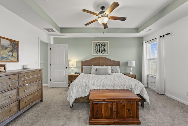 bedroom with baseboards, visible vents, a raised ceiling, and light colored carpet