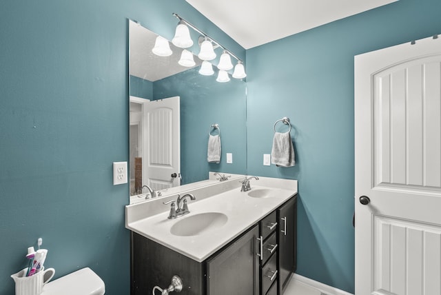 bathroom with baseboards, a sink, toilet, and double vanity