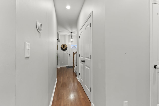 hallway with baseboards, arched walkways, and dark wood-style flooring