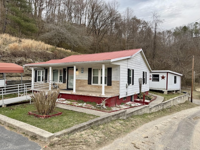 view of front of house featuring stone siding, metal roof, fence, and a porch