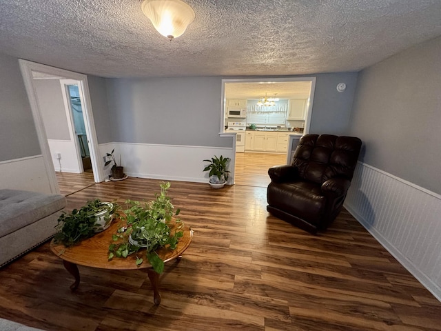 living area featuring a notable chandelier, a textured ceiling, wood finished floors, and wainscoting