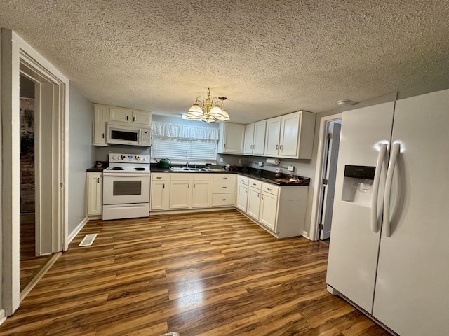 kitchen featuring dark wood finished floors, dark countertops, an inviting chandelier, white cabinetry, and white appliances