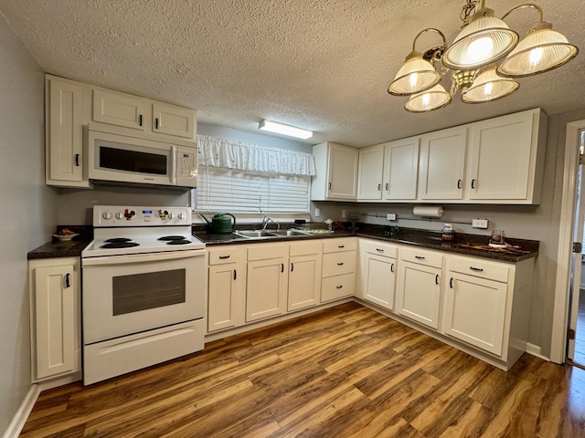 kitchen with white appliances, a sink, white cabinetry, dark countertops, and dark wood finished floors