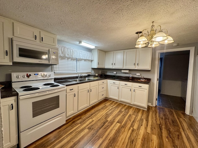 kitchen featuring white appliances, wood finished floors, a textured ceiling, white cabinetry, and a sink