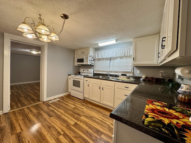 kitchen featuring white appliances, dark countertops, wood finished floors, white cabinetry, and a sink