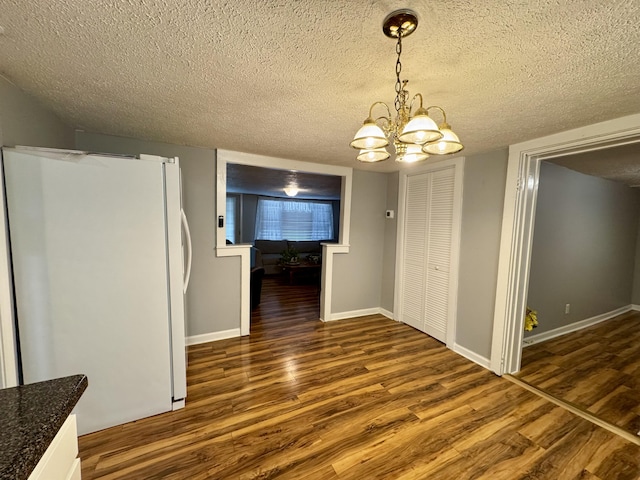 unfurnished dining area with a textured ceiling, a chandelier, wood finished floors, and baseboards