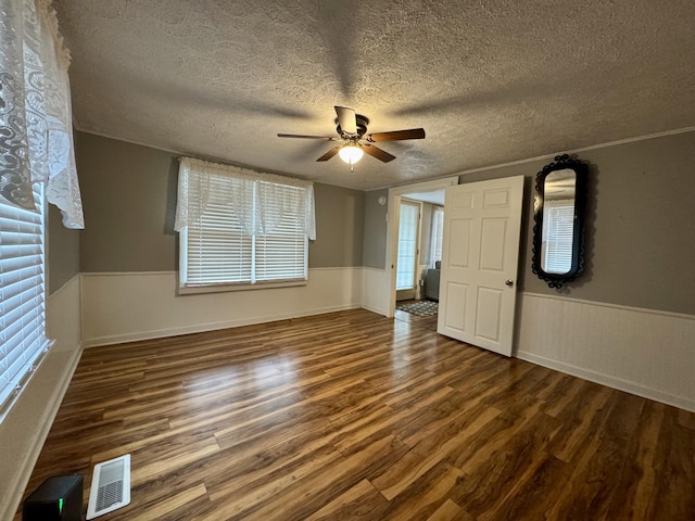 unfurnished bedroom featuring a wainscoted wall, visible vents, ceiling fan, a textured ceiling, and wood finished floors