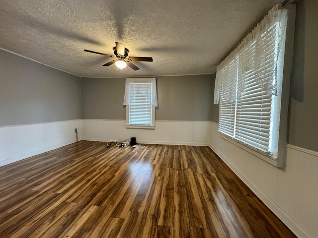 empty room with a wainscoted wall, a textured ceiling, wood finished floors, and a ceiling fan