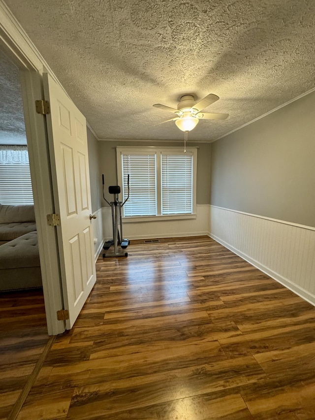 interior space featuring dark wood-style floors, crown molding, a ceiling fan, wainscoting, and a textured ceiling