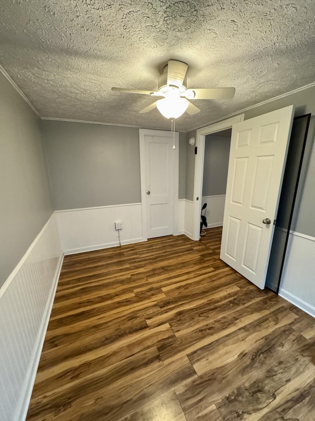 interior space with a wainscoted wall, a textured ceiling, dark wood finished floors, and a ceiling fan