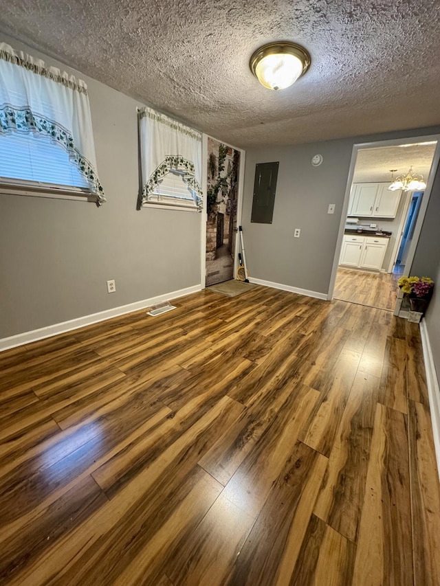 empty room featuring a textured ceiling, wood finished floors, electric panel, and baseboards