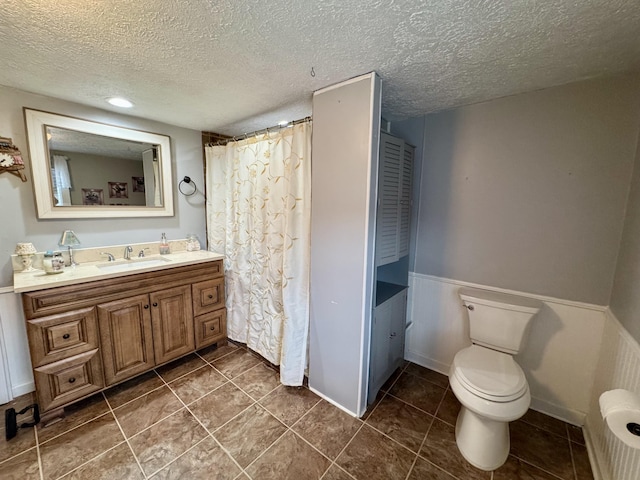 bathroom with wainscoting, toilet, tile patterned flooring, a textured ceiling, and vanity