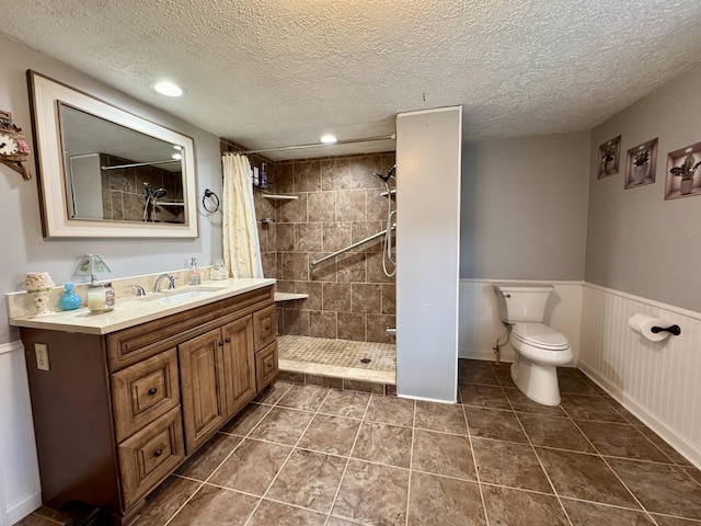 full bathroom featuring tiled shower, wainscoting, toilet, a textured ceiling, and vanity