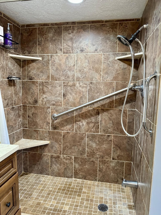 full bathroom featuring a tile shower, a textured ceiling, and vanity