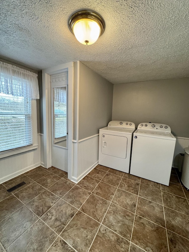 clothes washing area with visible vents, a wainscoted wall, washing machine and clothes dryer, a textured ceiling, and dark tile patterned floors